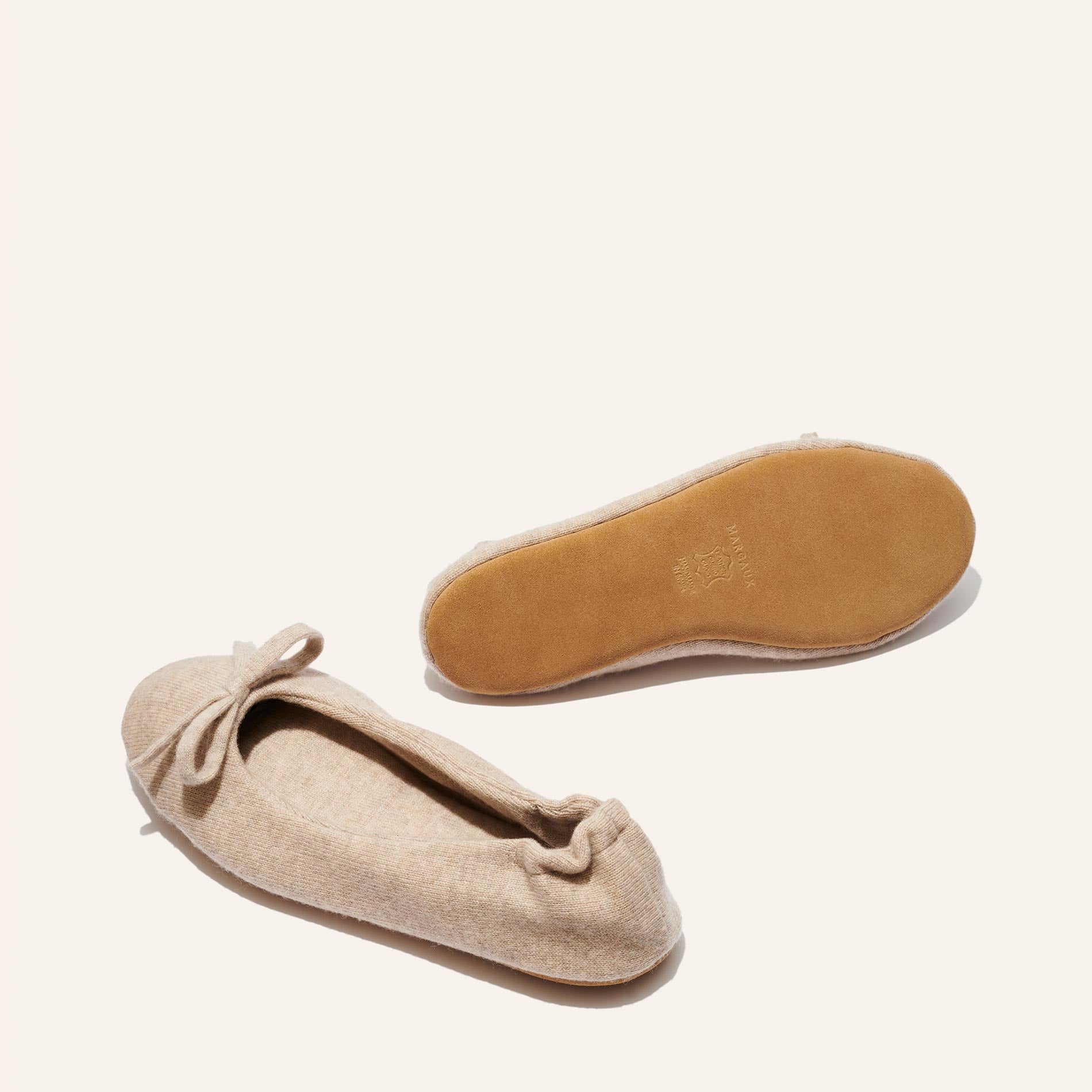 The Ballet Slipper - Oatmeal by Margaux: Beige wool-cashmere flats with a front bow. One shoe shows the side, the other displays the light brown sole—an ultra-soft, cozy choice for relaxing in style.