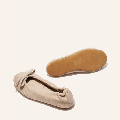 The Ballet Slipper - Oatmeal by Margaux: Beige wool-cashmere flats with a front bow. One shoe shows the side, the other displays the light brown sole—an ultra-soft, cozy choice for relaxing in style.