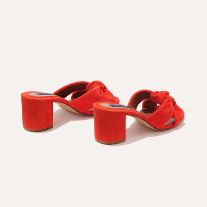 The Carmine Mule - Chili Suede by margaux-development: bright red open-toe heeled sandals featuring a plush knot design and block heel, combining comfort and style, displayed on a light background.