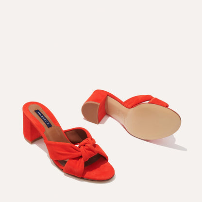 The Carmine Mule - Chili Suede by margaux-development is a vibrant red, open-toe block heel sandal featuring a plush knot bow and suede finish, shown from top and bottom on a white background for comfort and style.