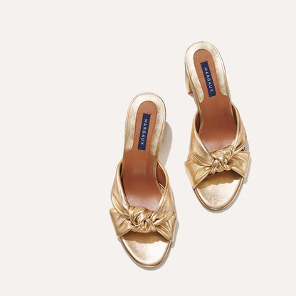 The Carmine Mule in shiny Gold Nappa, a slide-on heel featuring a plush knot detail and comfortable 2.5-inch block heel