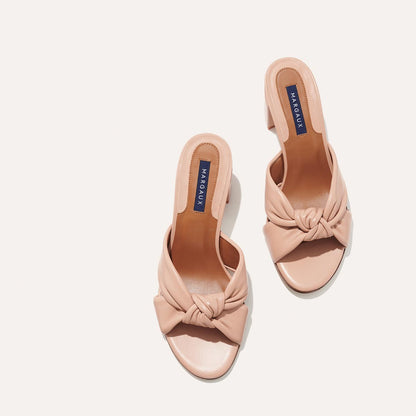The Carmine Mule - Rose Nappa by margaux-development features blush pink heeled sandals with plush knot, twisted front straps, open toes, block heel, and a MARGAUX insole label, shown on a light background.