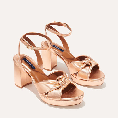 The Carmine Platform - Blush Metallic Nappa by margaux-development features plush knot front straps, chunky high heels, ankle buckle straps, and indigo blue Margaux labels on the insoles, shown on a light background.