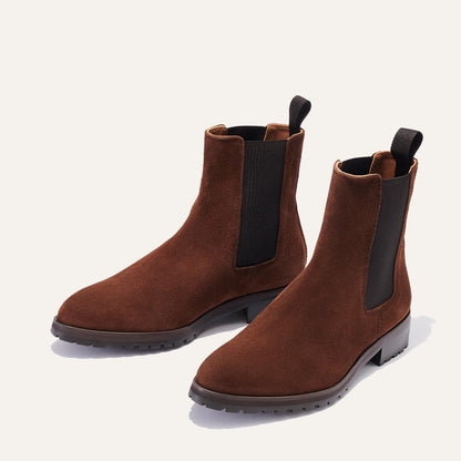 Margaux’s The Chelsea Boot in umber suede features black elastic side panels and pull tabs, showcased on a light background.