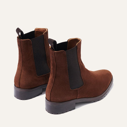 The Chelsea Boot - Umber Suede by Margaux: brown suede Chelsea boots with black elastic side panels and black pull tabs, shown from behind on a light background.