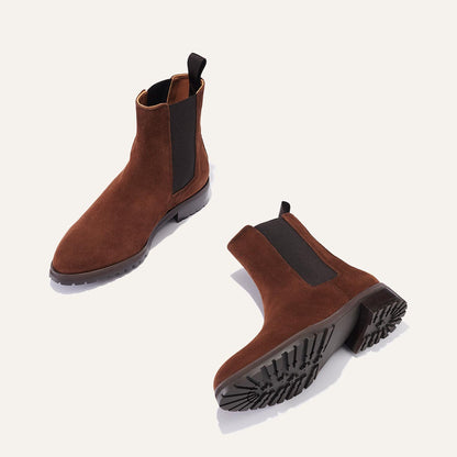 The Chelsea Boot - Umber Suede by Margaux: brown suede boots with black elastic side panels and chunky rubber soles, shown on a light background—one upright, the other on its side revealing the tread.