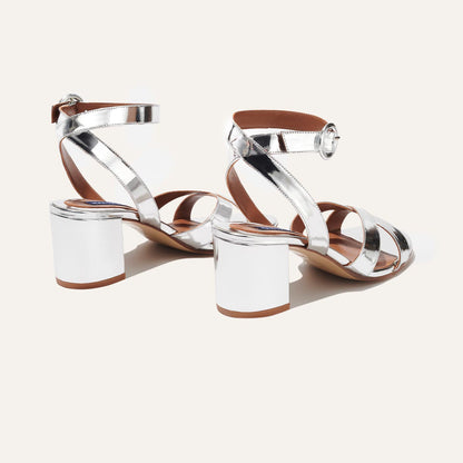 The City Sandal - Silver Mirror by margaux-development features shiny silver crisscross straps, ankle buckles, block heels, and a cushioned insole for comfort, displayed on a plain light background.