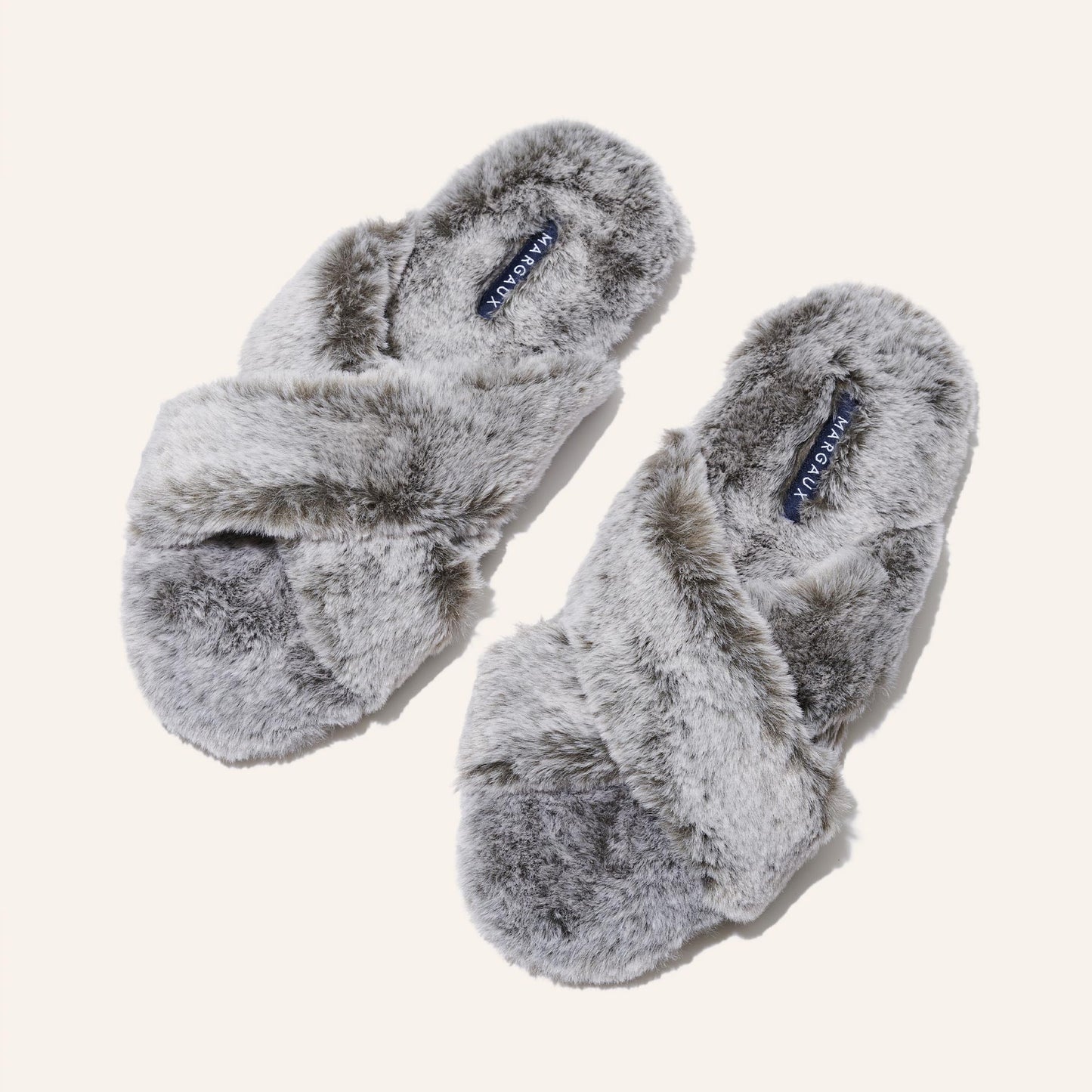 The Cozy Slipper - Grey by Margaux features a soft, fluffy texture and cozy x-strap design. This stylish faux fur slipper is displayed on a plain light background.