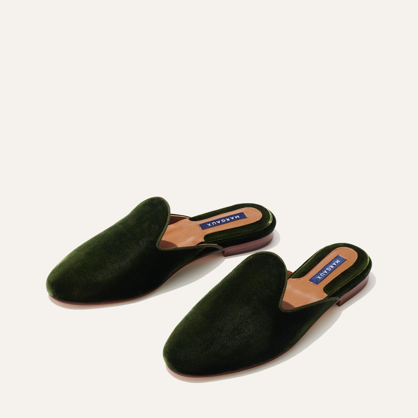 A pair of dark green velvet slip-on loafers with tan insoles and low brown heels, displayed on a light background.