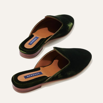 The Loafer Mule - Olive Velvet by Margaux features dark green velvet, brown soles, tan insoles with blue Margaux labels on the heel, and an almond toe design set against a neutral background.