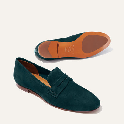 Margaux’s The Penny - Emerald Suede loafers feature dark green Italian suede and brown leather soles, shown with one shoe upright and the other on its side to highlight the unlined, glove-like fit and interior details.
