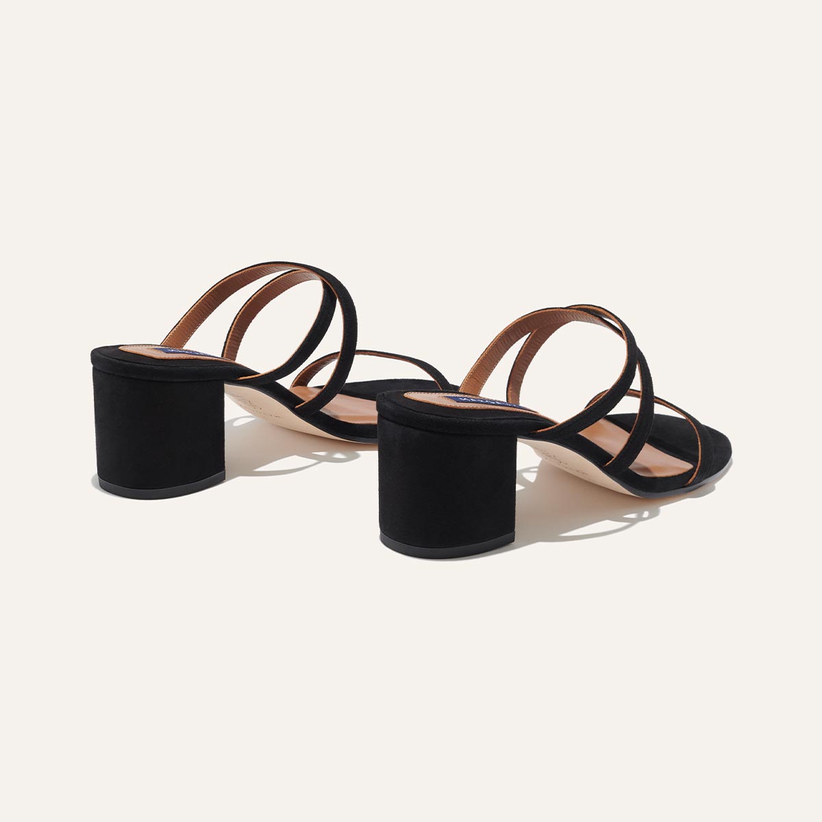 The Perry Sandal - Black Suede by margaux-development features black open-toe block heels with multiple thin straps and a chic suede upper, shown on a light background from a rear side angle.