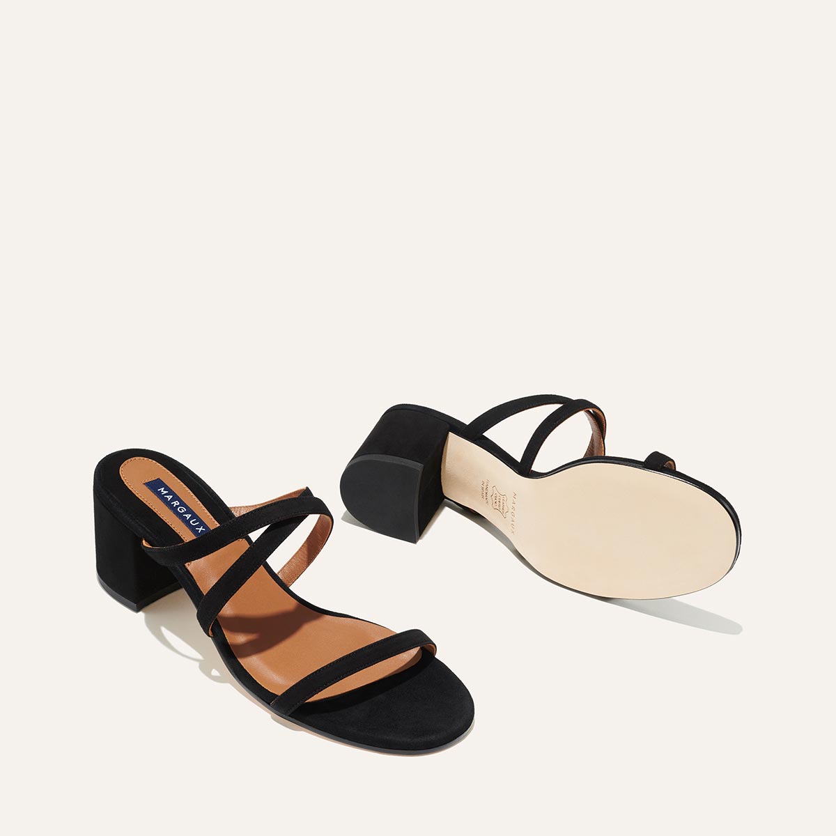 The Perry Sandal - Black Suede by margaux-development: a pair of black open-toe block heel sandals featuring suede uppers, three slim straps, tan insoles; one shoe is upright and the other reveals the sole.