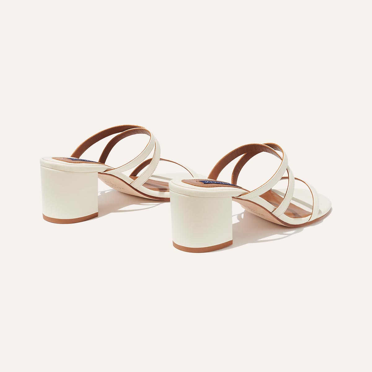 The Perry Sandal - Ivory Nappa by margaux-development features chunky block heels and thin crisscross straps, crafted from smooth Nappa leather, shown on a light background.