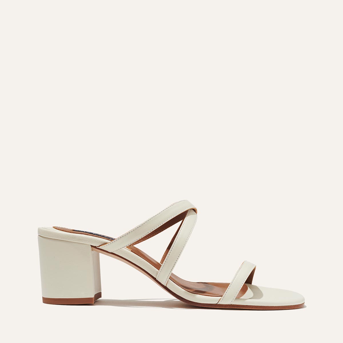 The Perry Sandal - Ivory Nappa by margaux-development features a cream block heel, soft Nappa leather, two front straps, and a diagonal strap, shown in side profile against an off-white background.