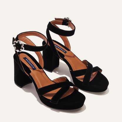 The Platform Sandal - Black Velvet from margaux-development features black velvet with block heels, ankle and cross-toe straps, tan insoles, and silver buckles for stylish comfort, shown on a light background.