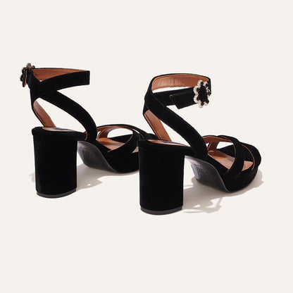 The Platform Sandal - Black Velvet by margaux-development features black velvet, thick heels, crisscross and ankle straps with decorative buckles, offering stylish comfort. Displayed on a plain light background.