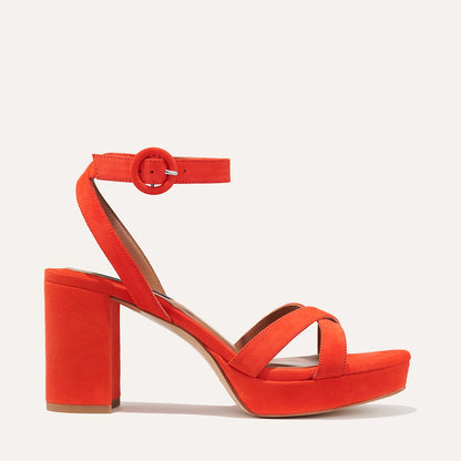 The Platform Sandal - Chili Suede by margaux-development features bright red suede, a chunky block heel, ankle strap with round buckle, and crisscross toe design, shown in profile on a plain background.