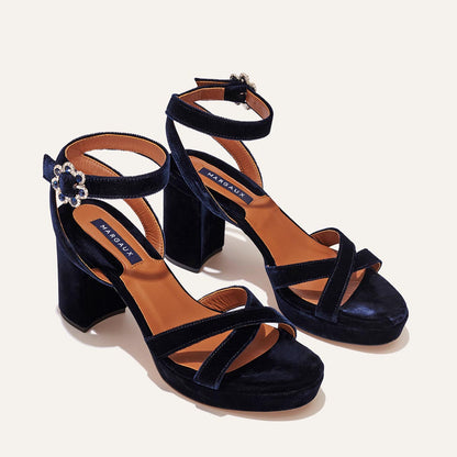 The Platform Sandal by margaux-development features midnight blue velvet, thick heels, tan insoles, crisscross front straps, and ankle straps with jeweled flower-shaped buckles.
