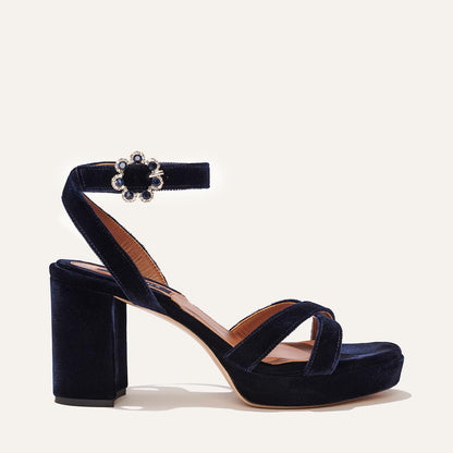 The Platform Sandal by margaux-development features midnight blue velvet, thick straps, a chunky block heel, platform sole, and an ankle strap with a jeweled floral buckle.