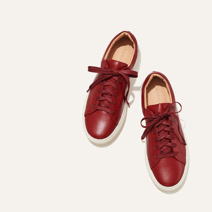 A pair of The Sneaker - Burgundy Calf by margaux-development, featuring burgundy leather, white soles, and matching laces, placed side by side on a light background.