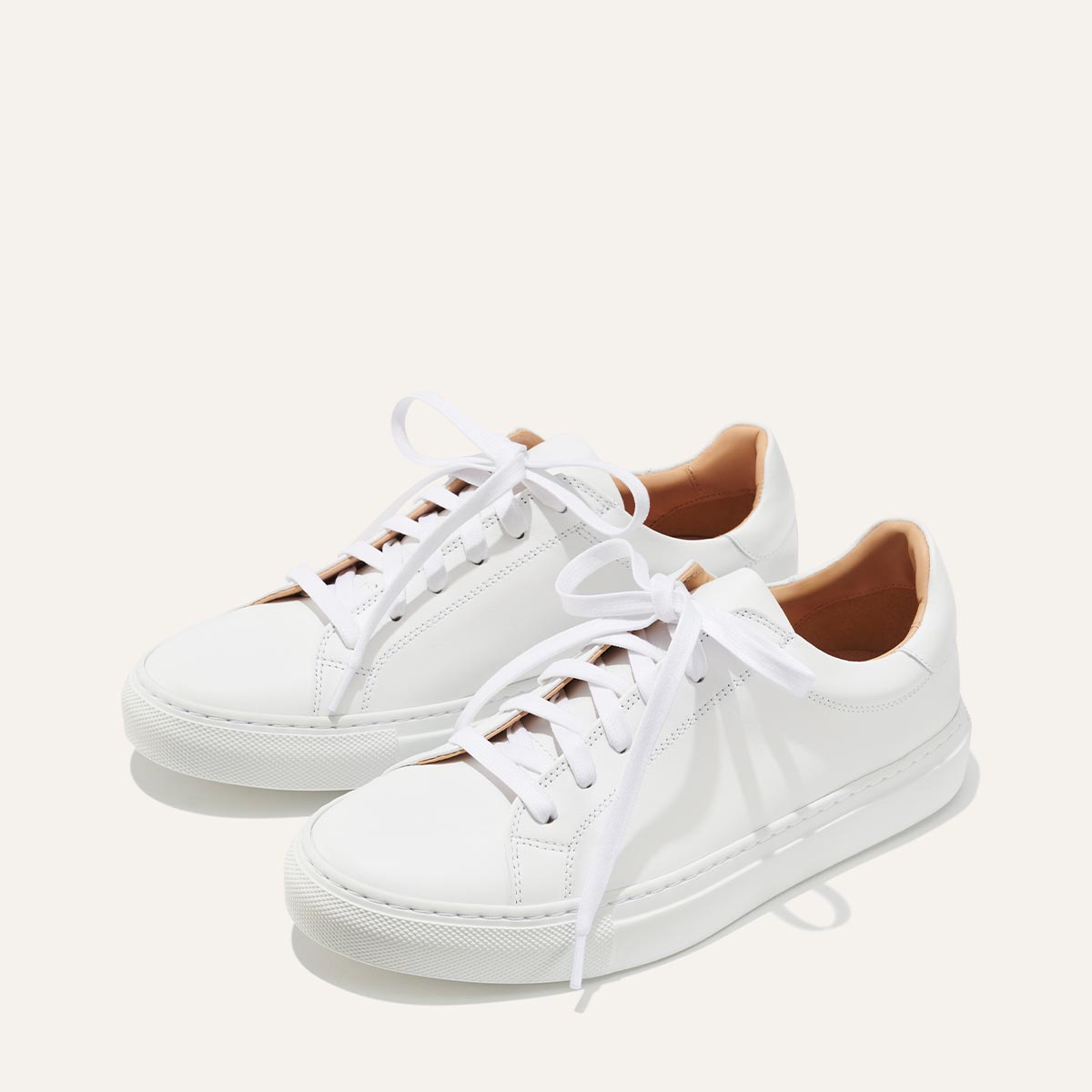 The Sneaker - White Calf by margaux-development: white low-top sneakers with white laces and a tan lining, shown on a plain light background.