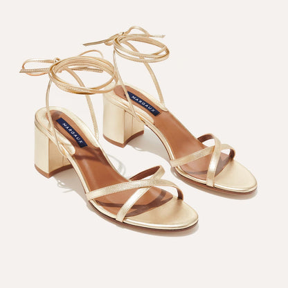 The Soho Sandal - Champagne Nappa by margaux-development features gold strappy block heels with ankle ties and open toes. These chic summer wrap sandals have a subtle sheen and are shown against a neutral background.