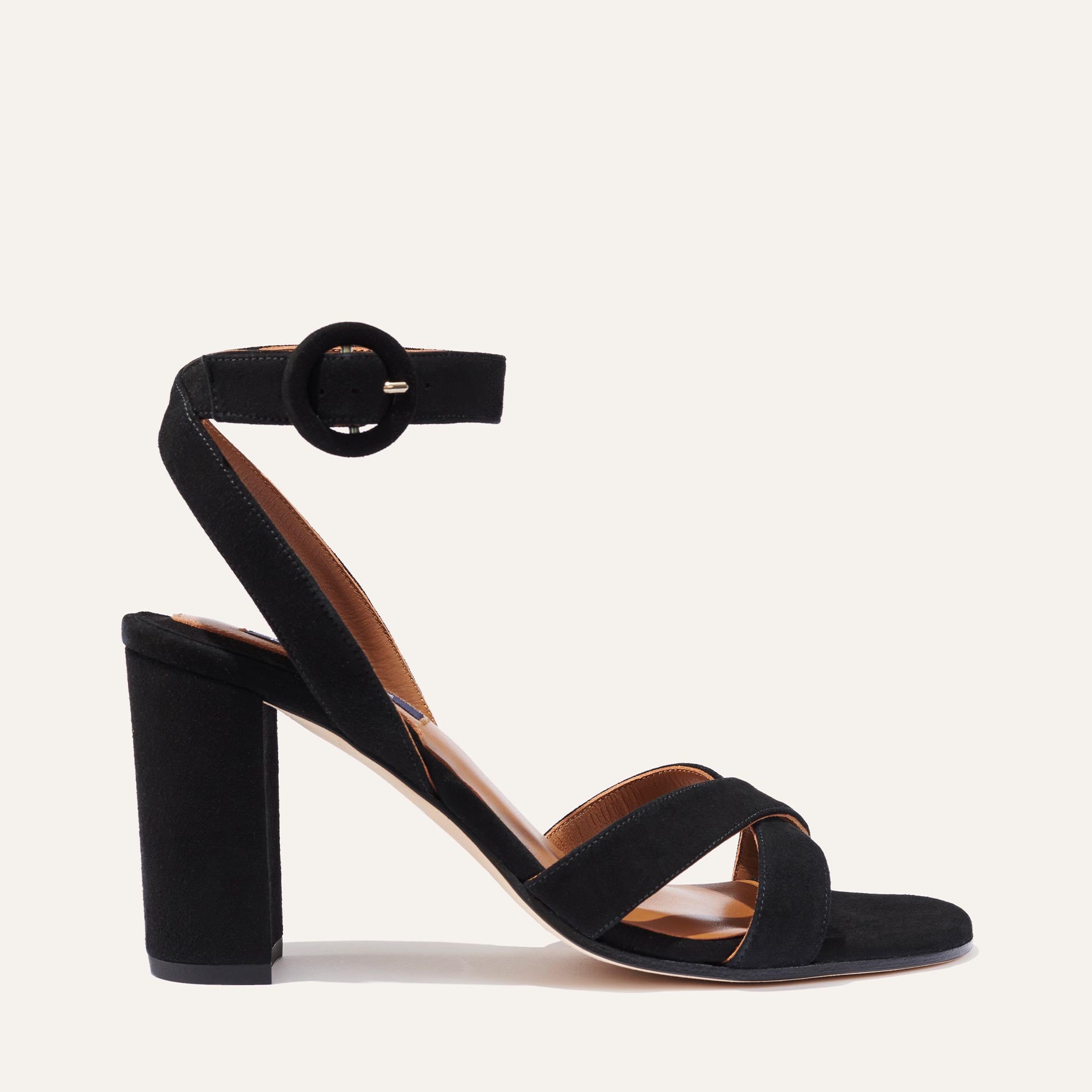 The Uptown Sandal - Black Suede by margaux-development features a black suede high block heel, ankle strap with round buckle, and two crisscrossing front straps—perfect for all-day comfort and versatile city style.