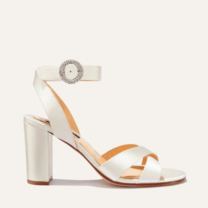 The Uptown Sandal - Ivory Satin with Crystal Buckle by margaux-development features a chunky block heel, crisscross satin toe straps, and an ankle strap with a jeweled buckle—perfect for elegant style and all-day comfort.