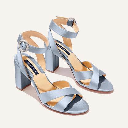 The Uptown Sandal by margaux-development features powder satin, an open toe, block heel, crisscross and ankle straps with a crystal buckle, cushioned insoles for comfort, and a blue Margaux label on the beige insole.