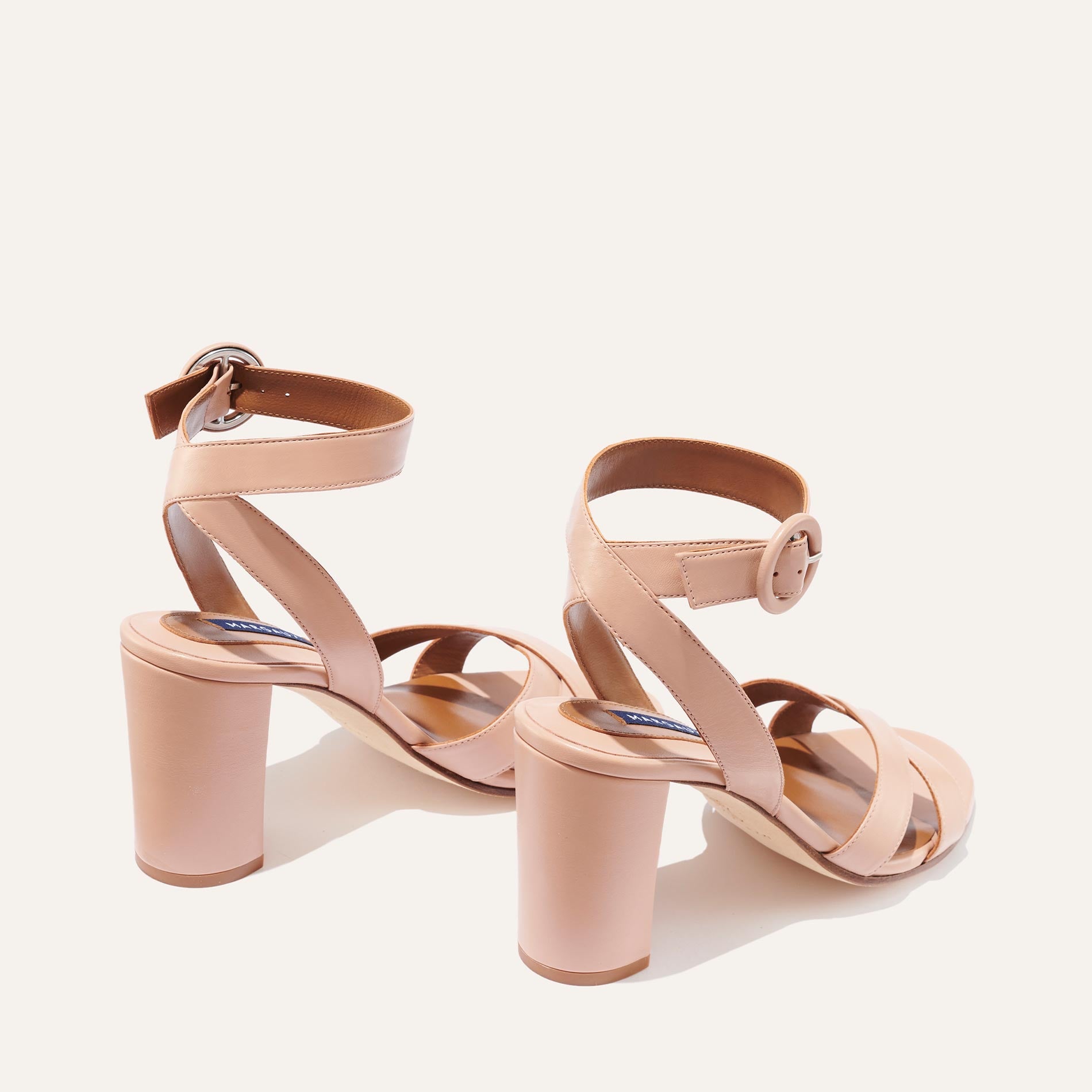 The Uptown Sandal - Rose Nappa by margaux-development features nude block heels, crisscross toe straps, and ankle straps with round buckles—delivering all-day comfort and effortless style on a light background.